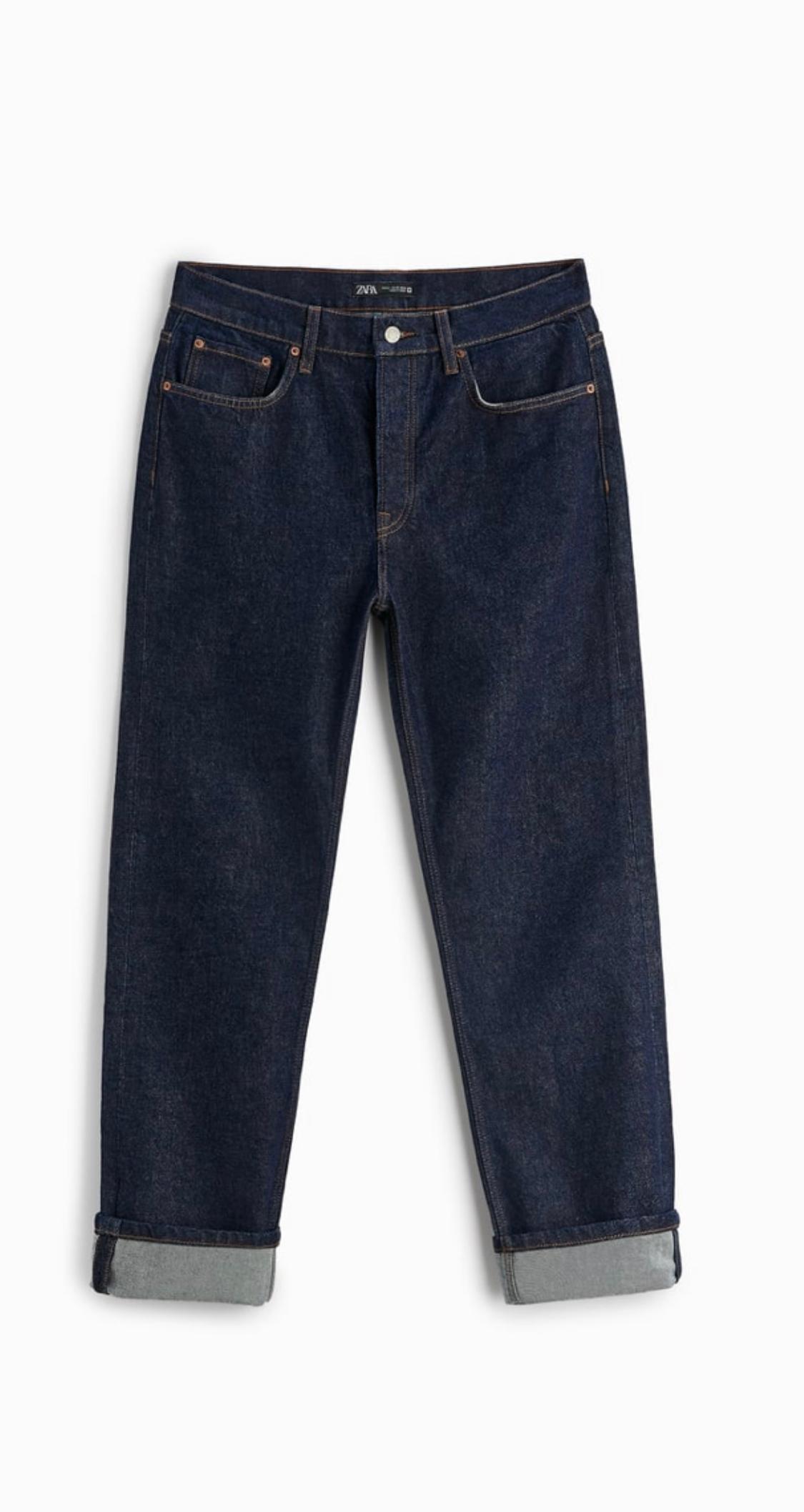 Front view of dark blue jeans with front and back pockets, metal button and turned-up hem.