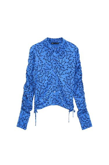 Blue long-sleeved shirt with a black floral print. Designed with a collar, button closure, gathered sleeves, and drawstrings at the hem.