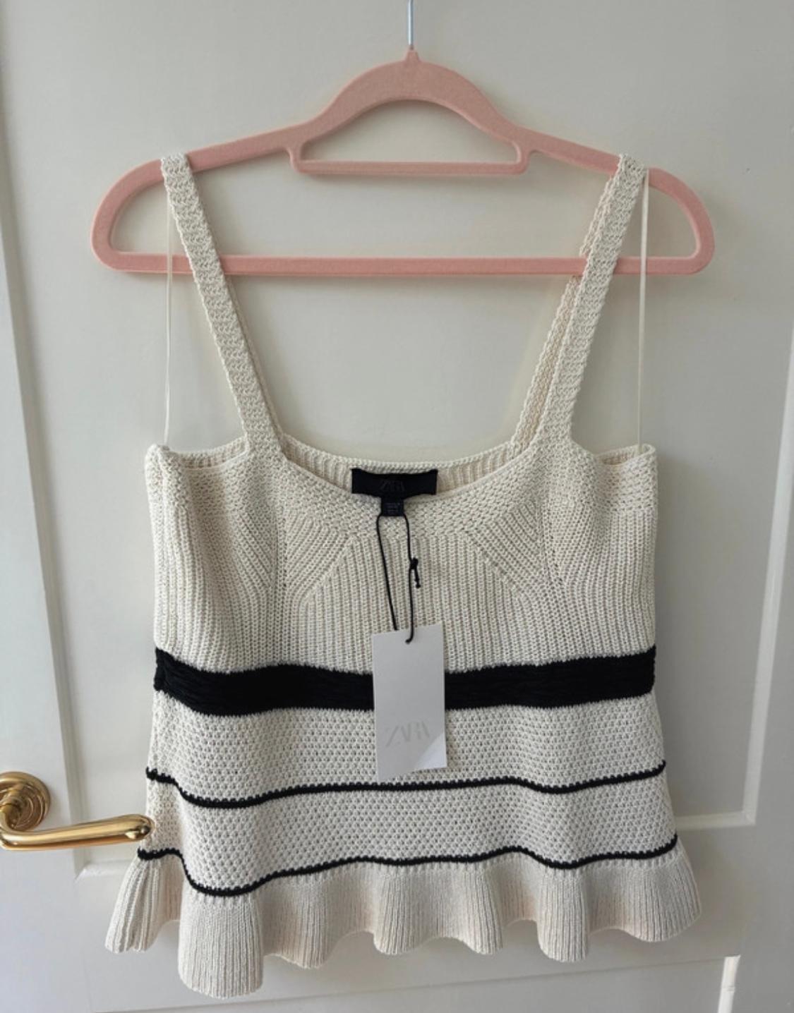 White knitted camisole with black stripes, hanging on a pink hanger. Visible label with the text "ZARA".