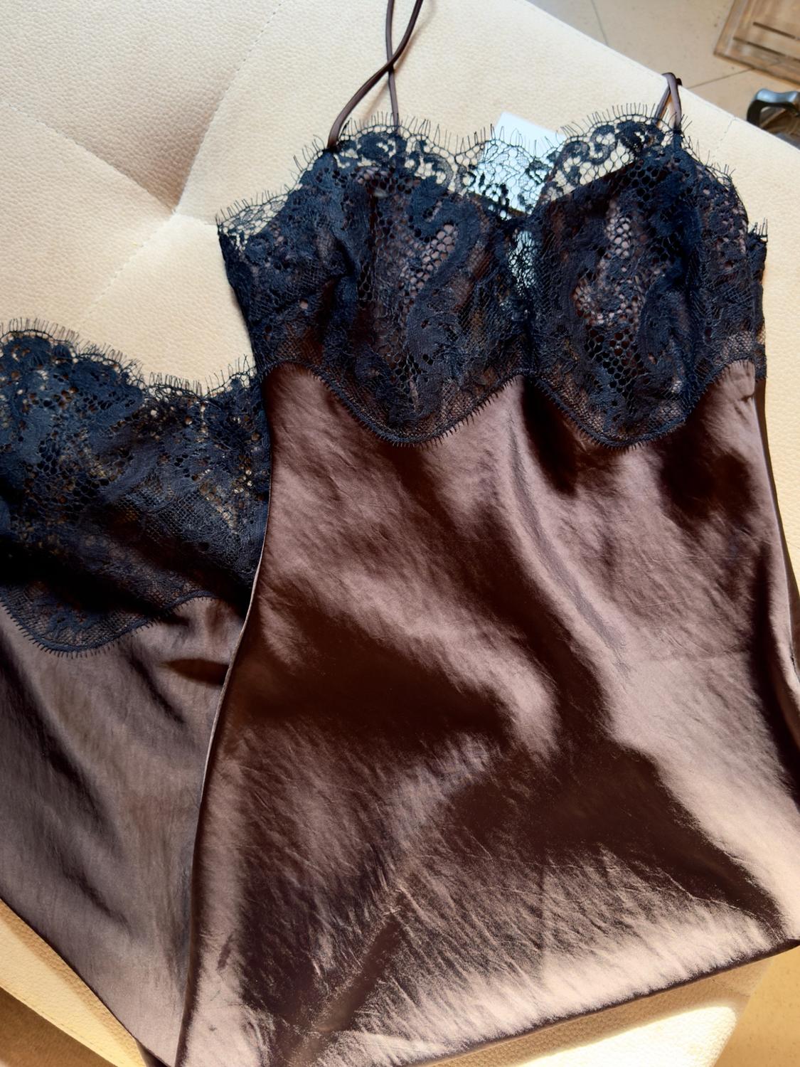 Brown satin slip dress with black lace at the neckline and delicate straps, on a beige surface. Relaxed and elegant style.