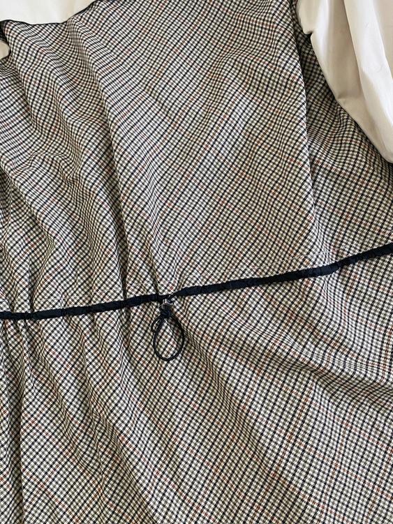 Small checkered pattern fabric in brown and black tones, with an adjustable black cord in the center. Visible white background.