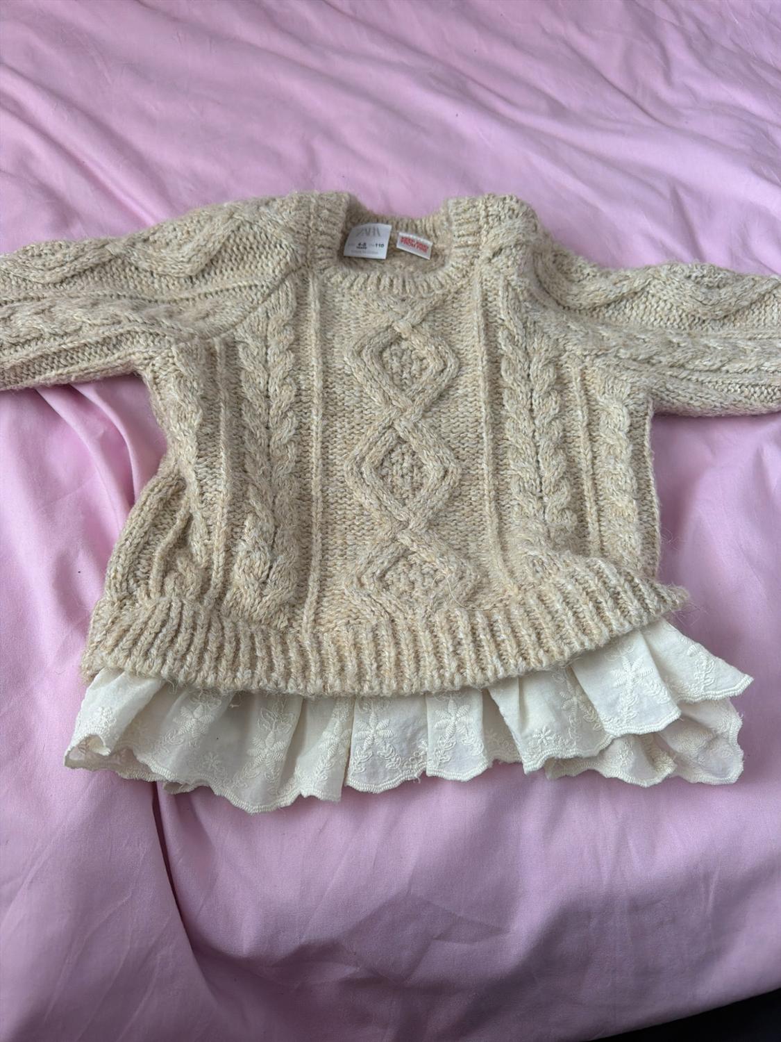 Beige cable-knit jumper with a white ruffled hem over a pink fabric. Visible ZARA label on the neck.
