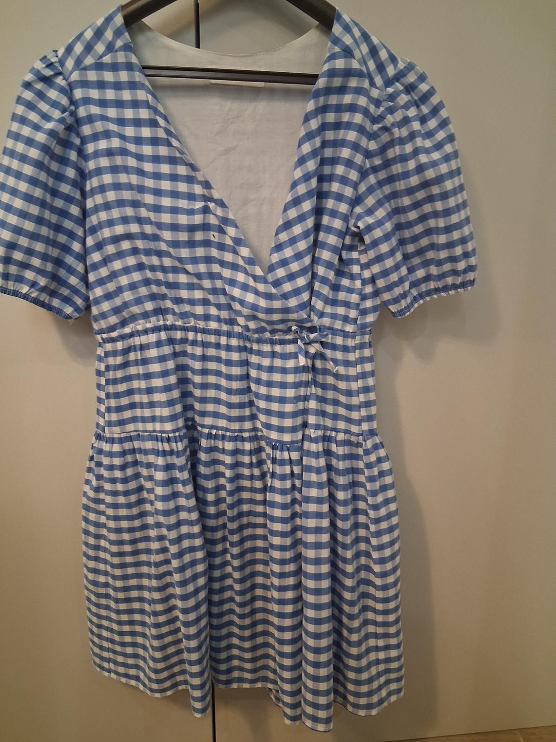 Blue and white checked dress with short puff sleeves and V-neck, hanging on a hanger against a neutral background.