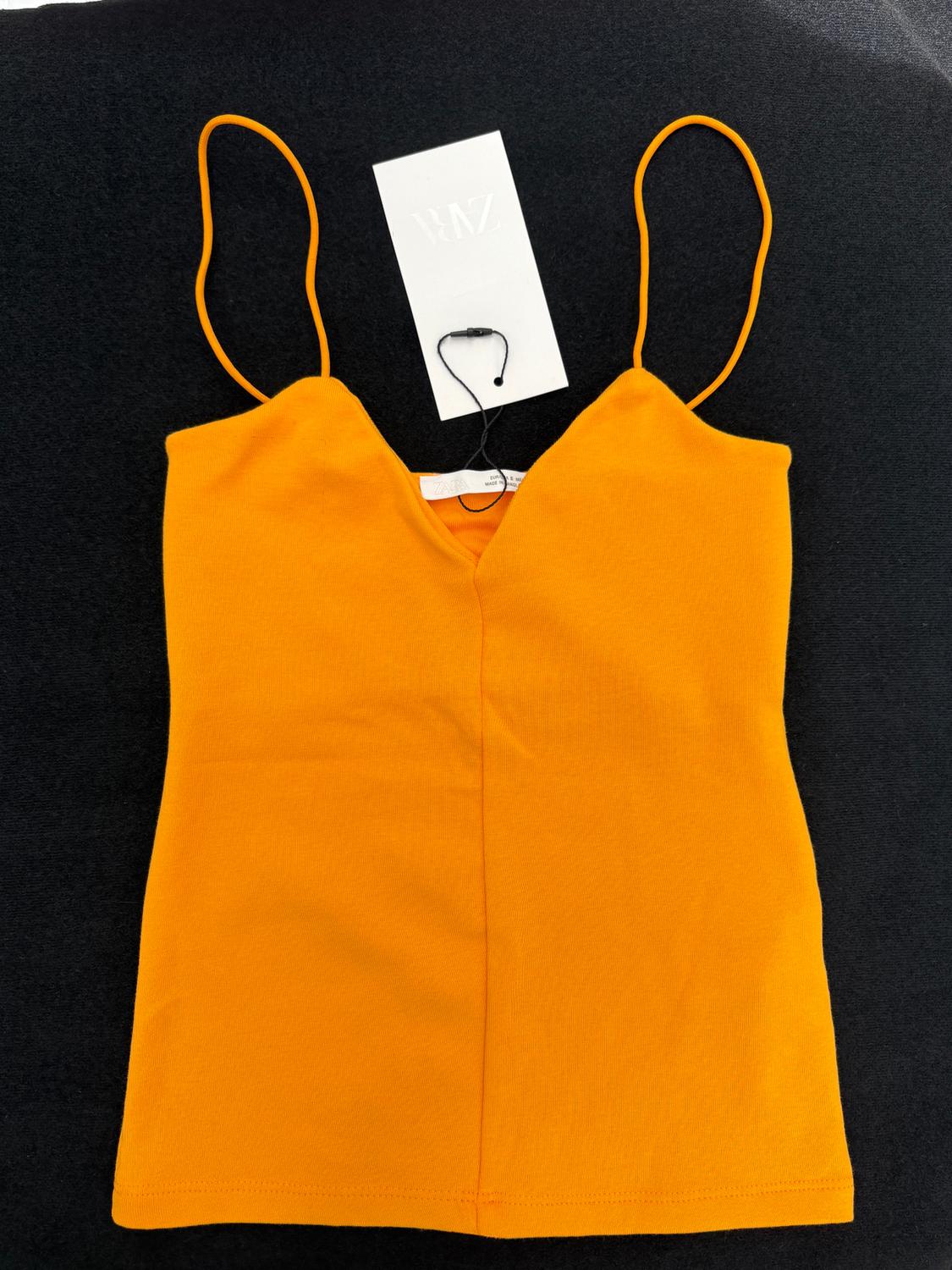 Orange camisole top on a black background, with a white label and black cord.