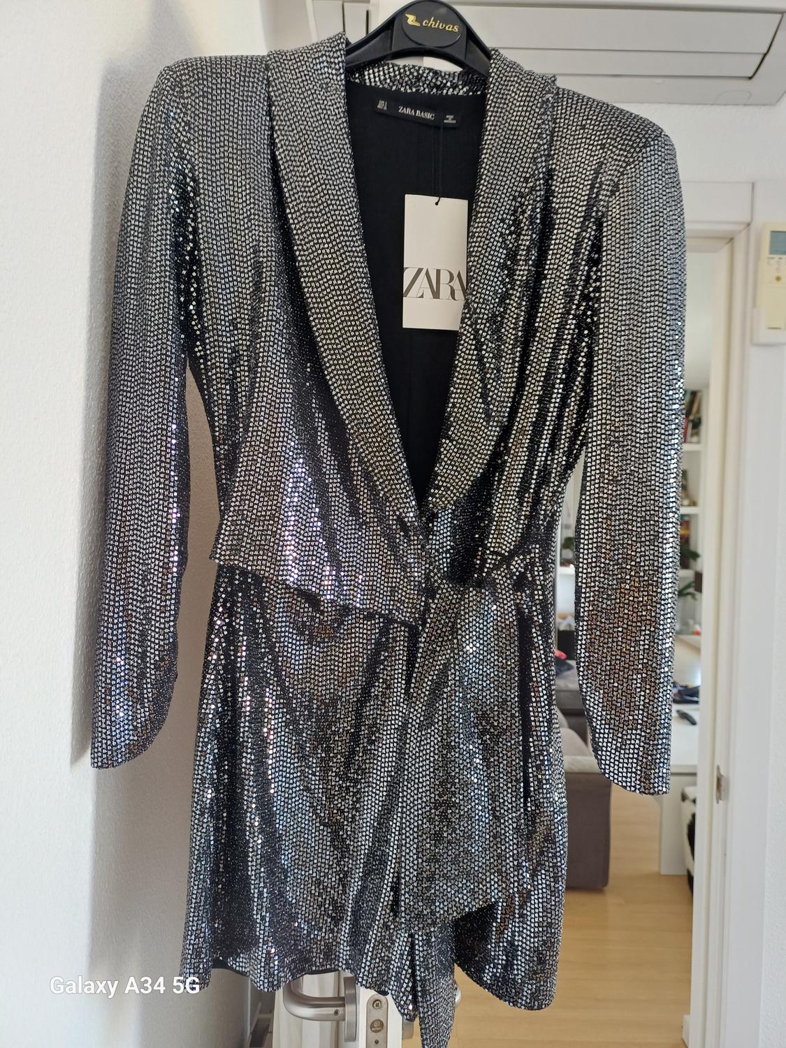 Shiny silver sequined short dress, hanging on a black hanger. Visible label with the text "ZARA". Text "Galaxy A34 5G" in the corner.