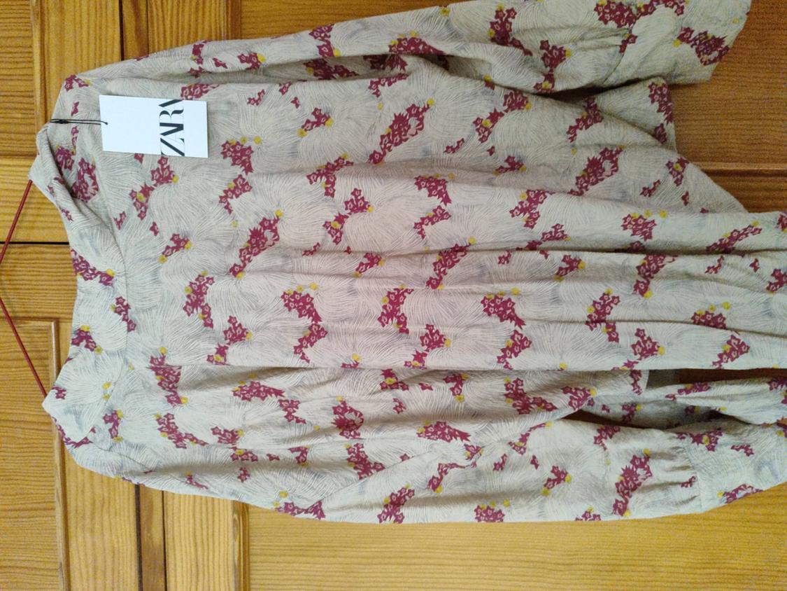Red and yellow floral print shirt on a beige background, hanging on a wooden hanger. Visible label with text "ZARA".