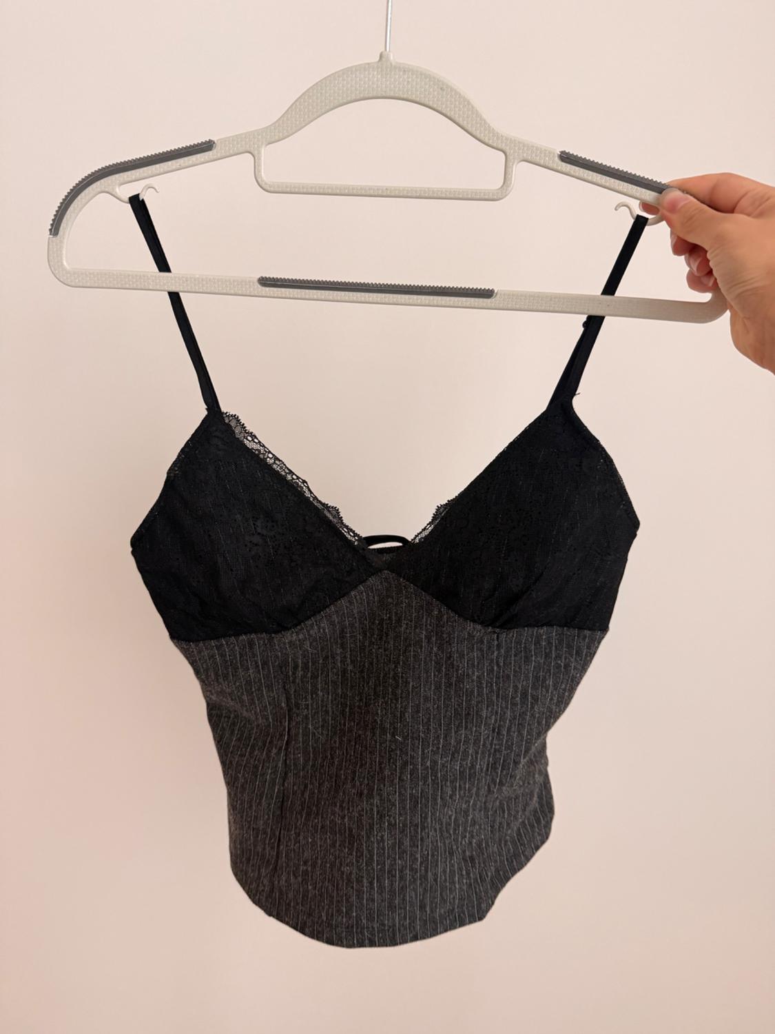 Hand holding a hanger with a spaghetti strap top. Black lace bust and gray body with thin vertical white stripes. Light background.