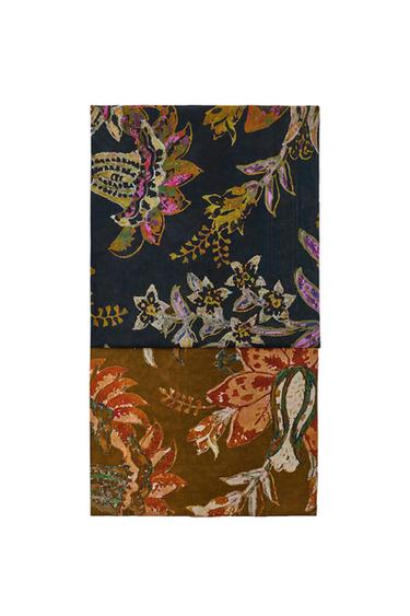 Two folded fabrics with a floral print. The top one has a dark background with colourful flowers and the bottom one is brown with orange motifs.
