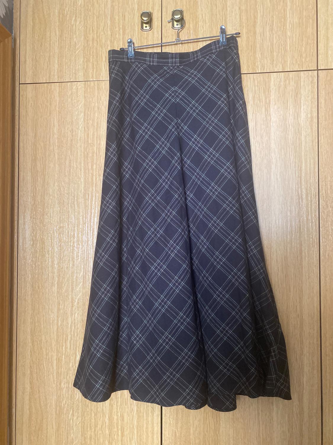 Dark checked trousers hanging on a hanger against a light wooden background.