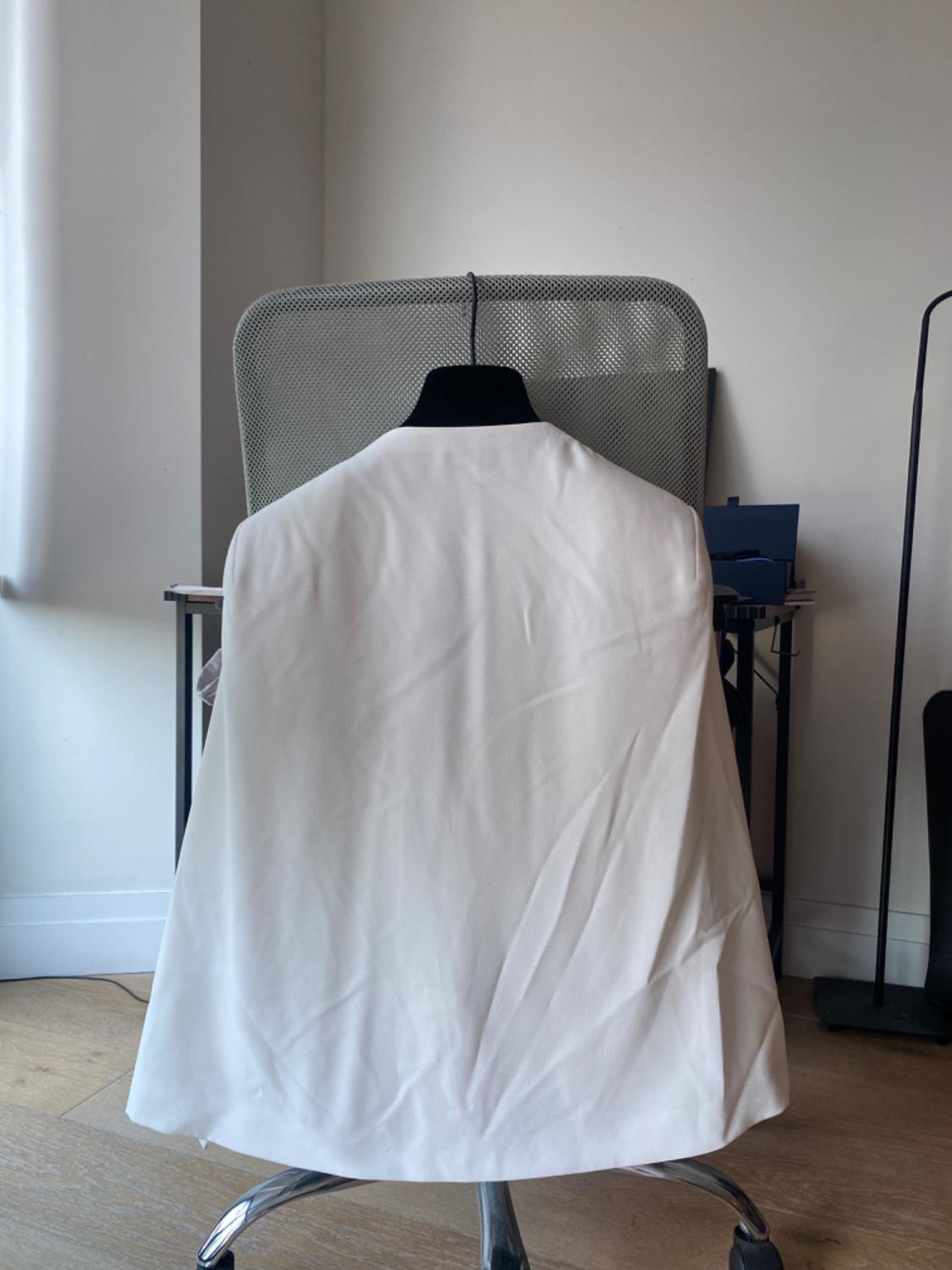 White jacket on a hanger on a grey office chair, in a room with a wooden floor and a desk.