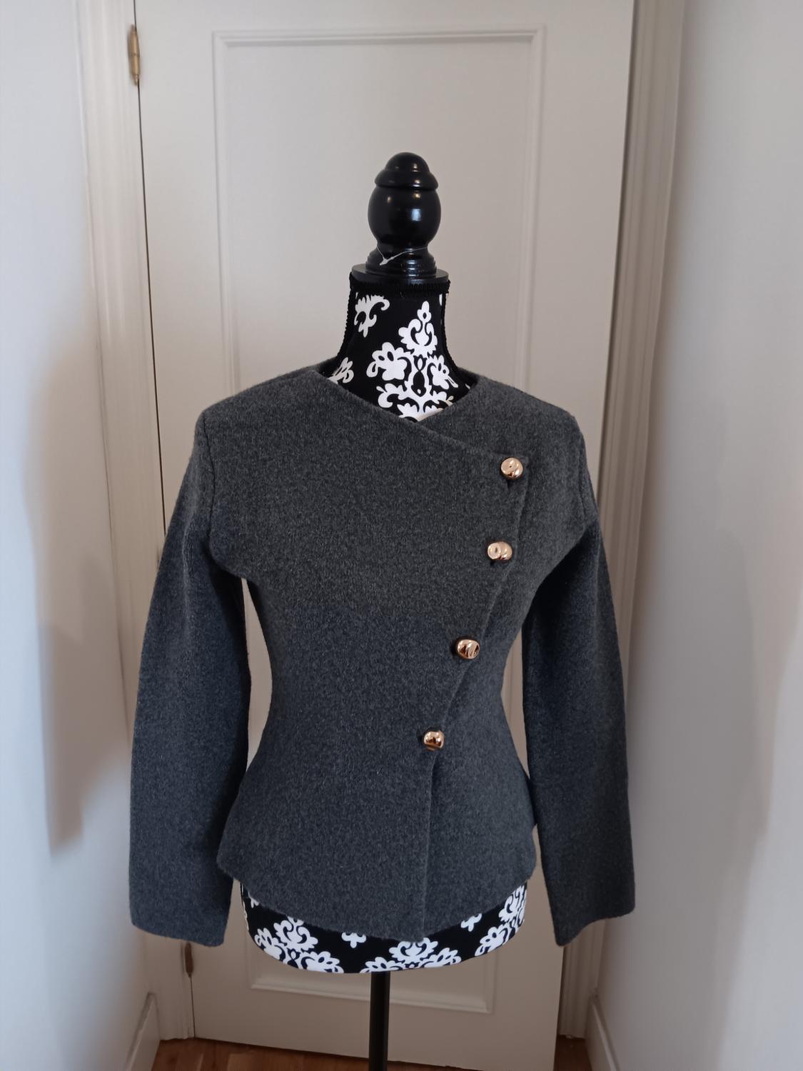 Grey jacket with gold buttons on a mannequin with a black and white design, white door background.