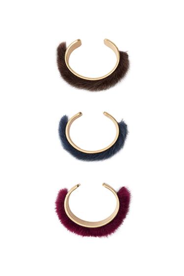 Three furry wristbands in brown, blue, and burgundy on a black background.