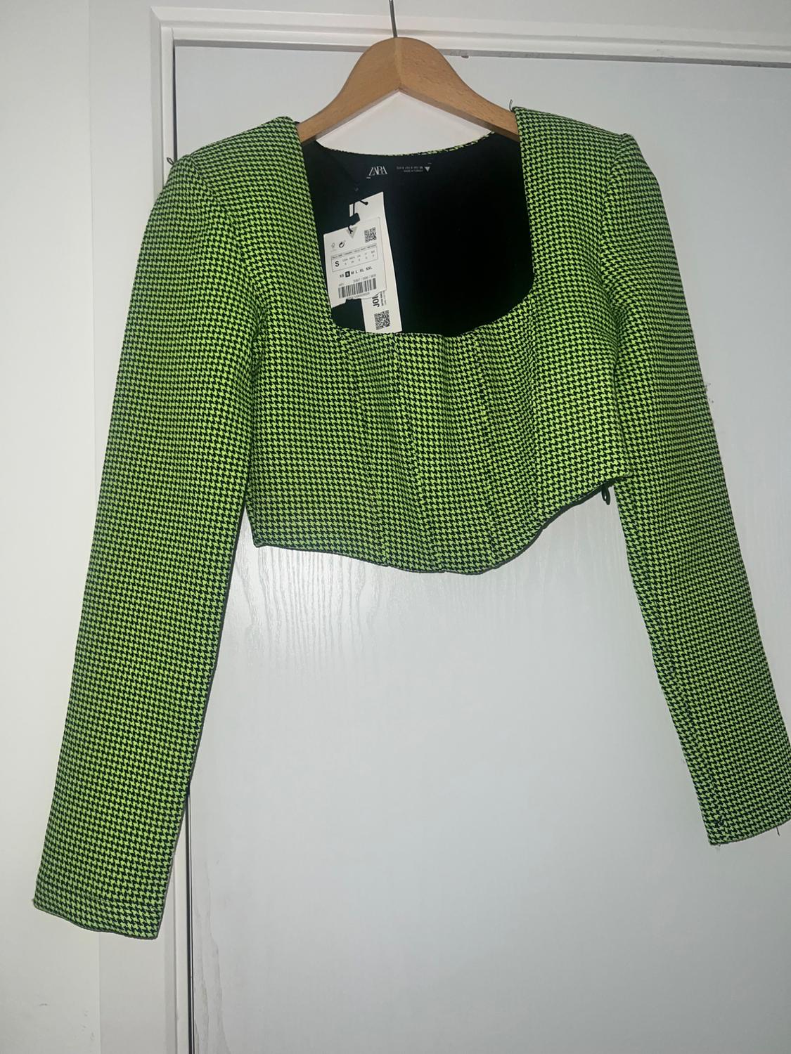 Long-sleeved crop top, green and black houndstooth print, square neckline. Hanging on a hanger on a white door. ZARA label.