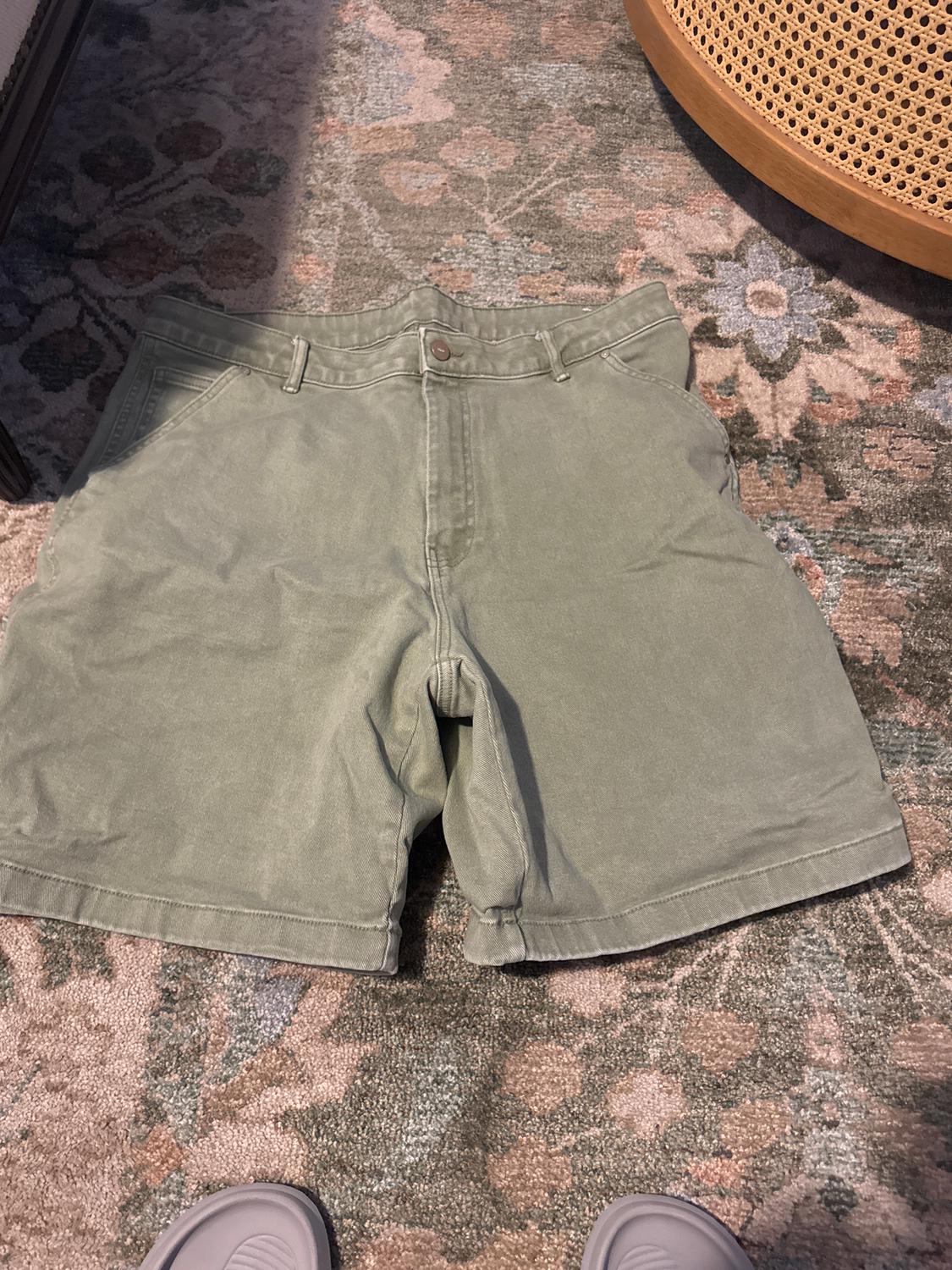 Olive green shorts on a floral patterned rug. Part of a wicker chair visible in the top right corner.
