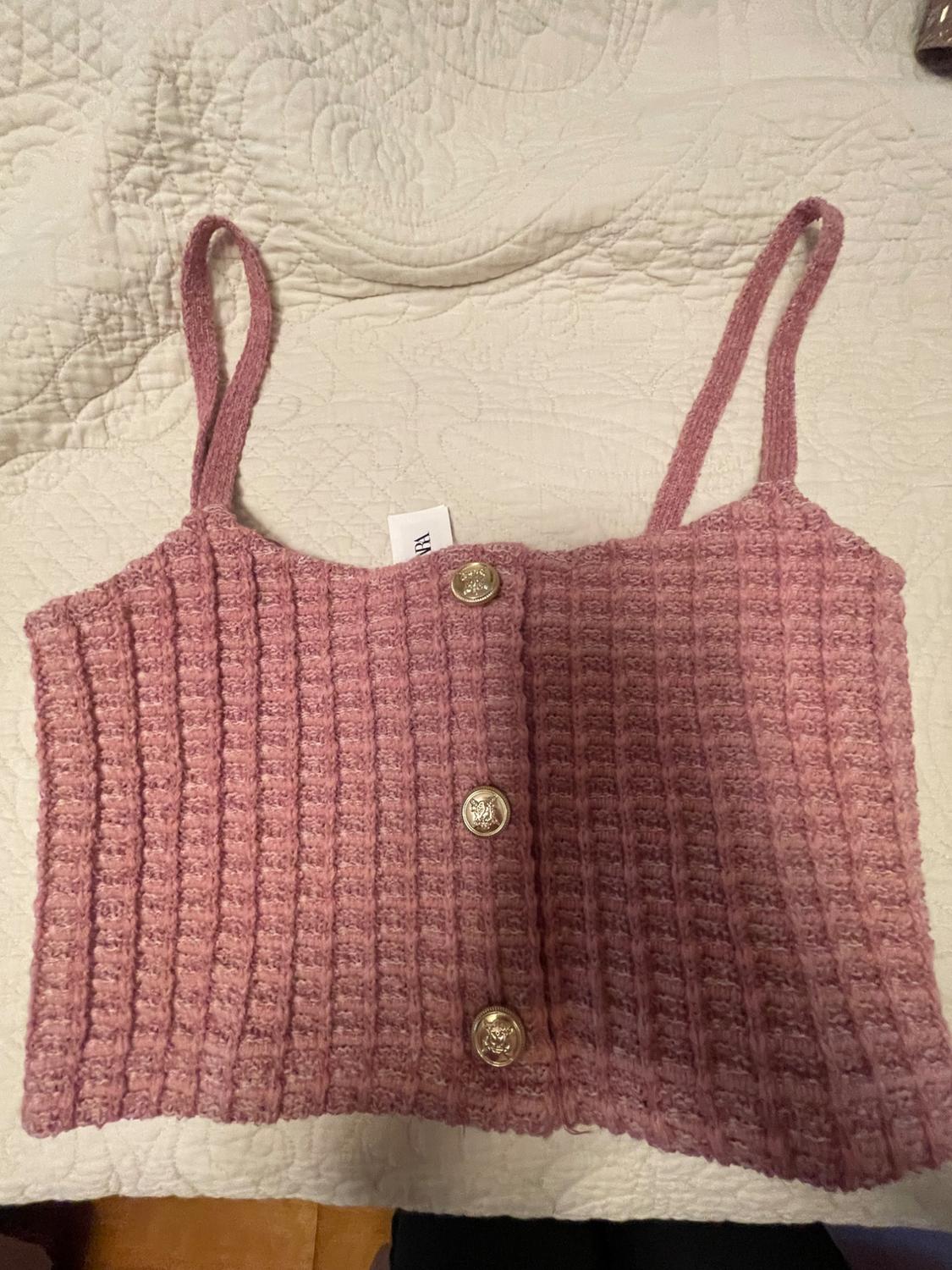 Pink knitted camisole top with decorative gold buttons on a white embossed bedspread.