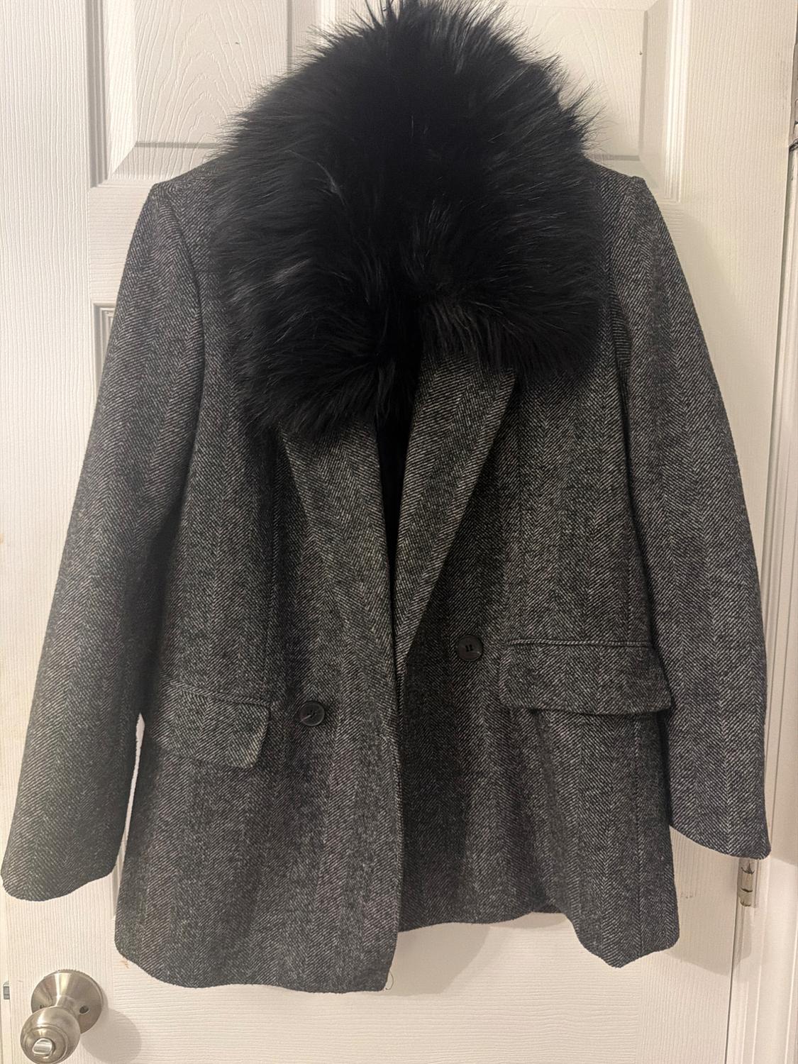 Gray herringbone coat with a black fur collar hanging on a white door.