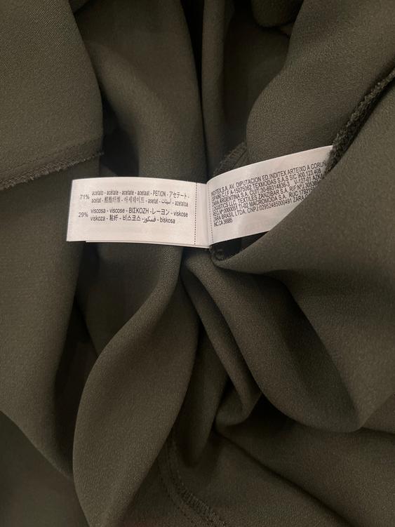 Dark green fabric with composition labels in various languages, including "71% acetate" and "29% viscose", on a crumpled background.