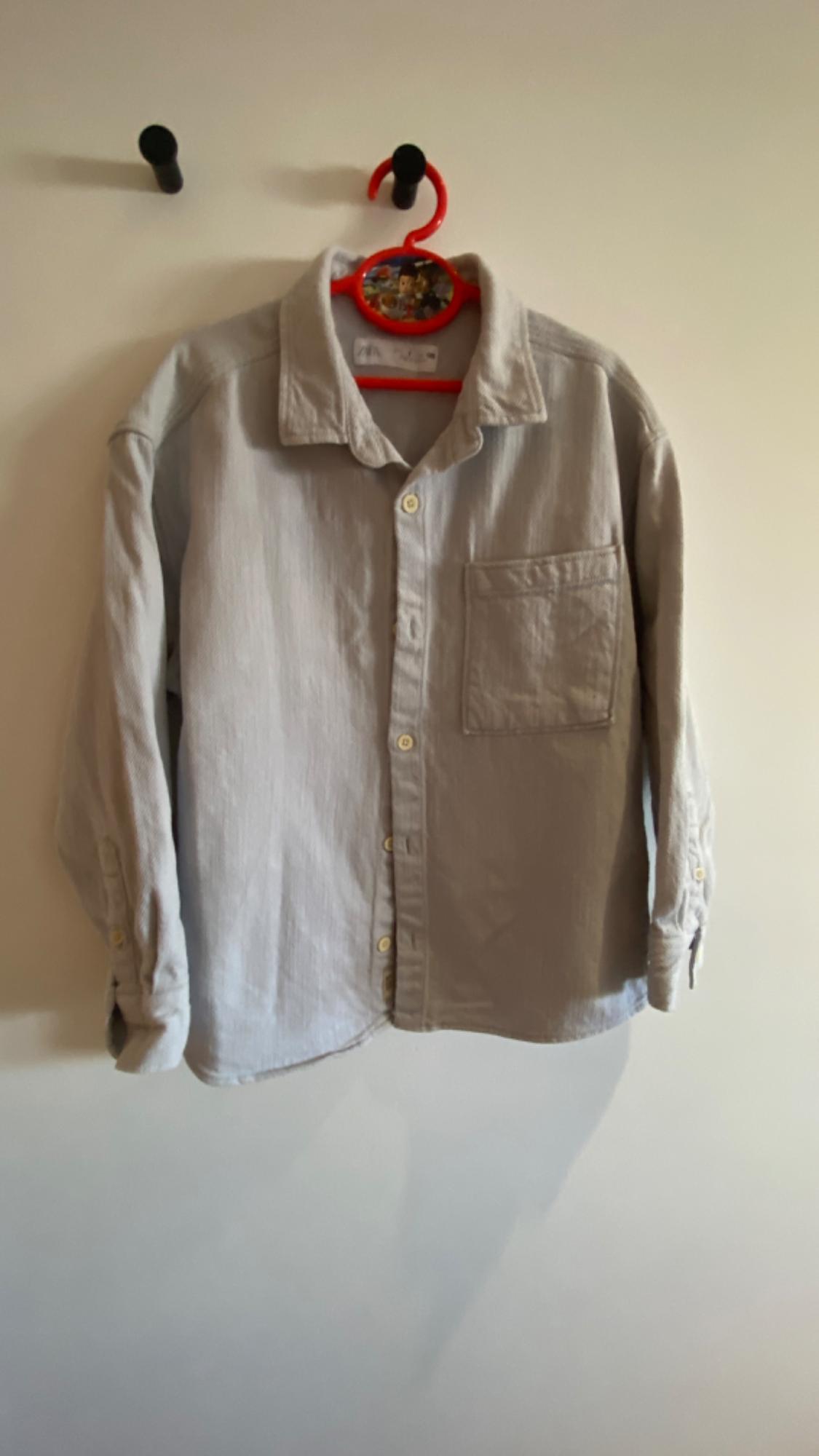 Light grey long-sleeved shirt hanging on a red hanger with cartoon details, against a white background.