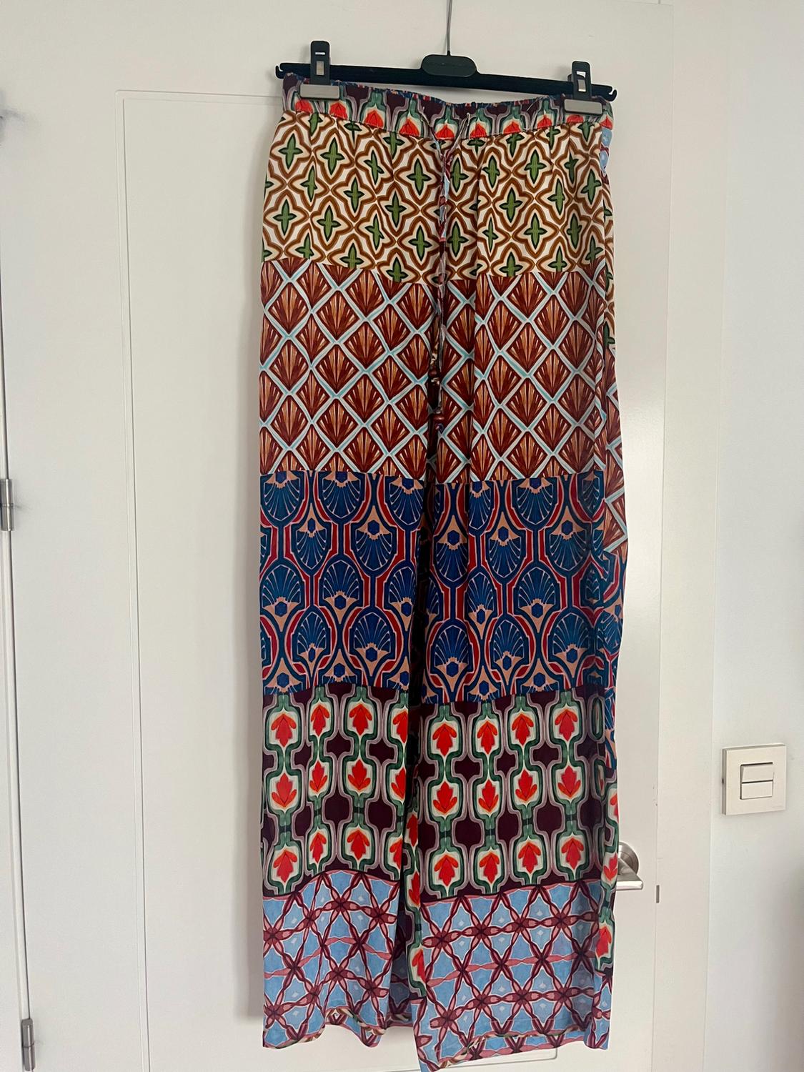 Hanging trousers with geometric and floral print in shades of brown, blue, red and green on a white background.