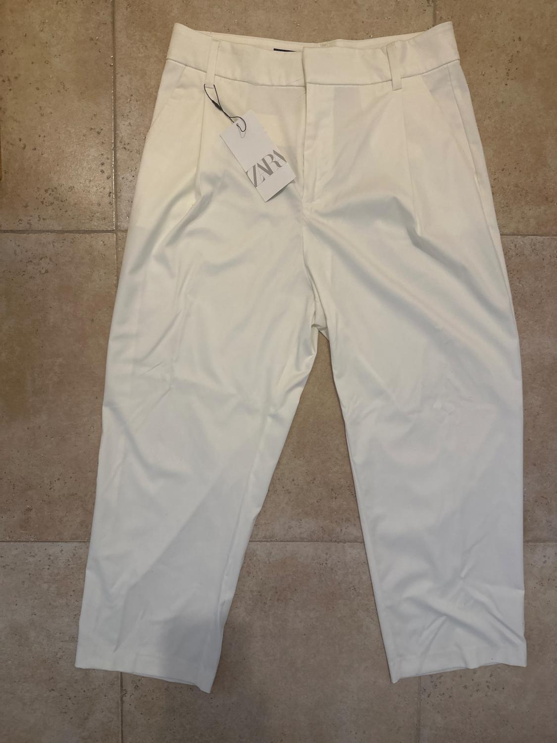 White trousers on a beige tiled floor, with a hanging tag that reads "ZARA".
