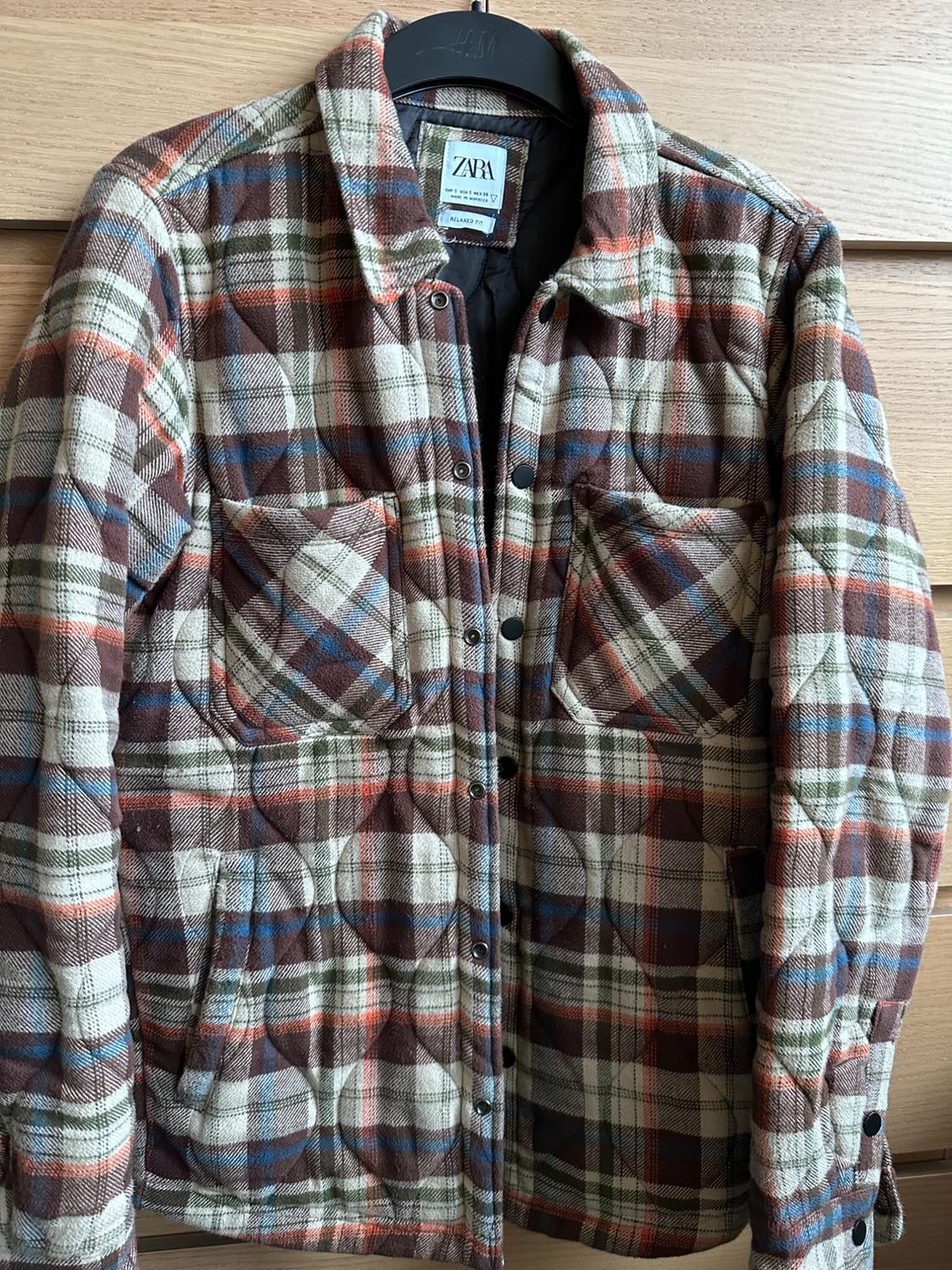 Brown, blue, and orange checked padded jacket hanging on a black hanger. Visible label: "ZARA".