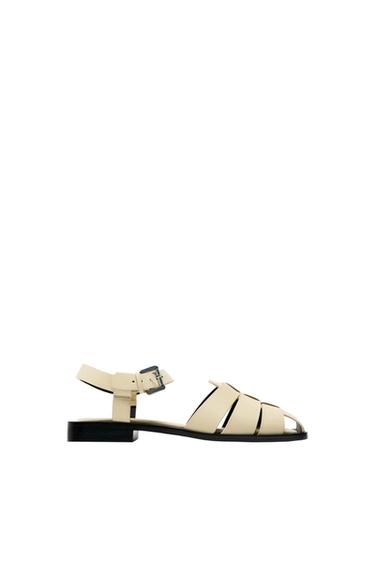 Side view of beige sandal with straps and metal buckle.