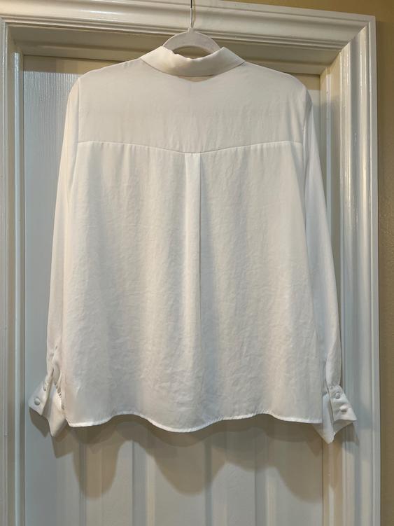 White long-sleeved shirt hanging on a door, seen from behind. Button detail on the cuffs.