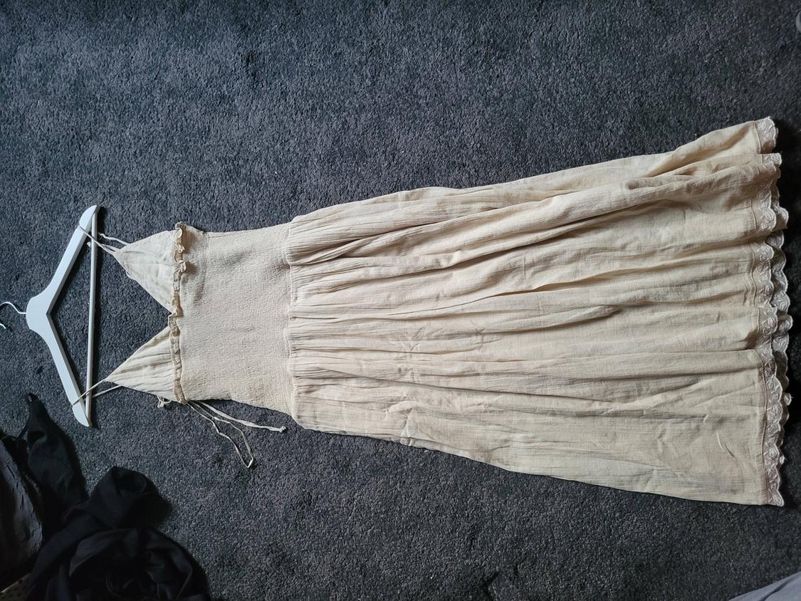 Beige maxi dress with thin straps and lace trim, on a white hanger on a grey rug.