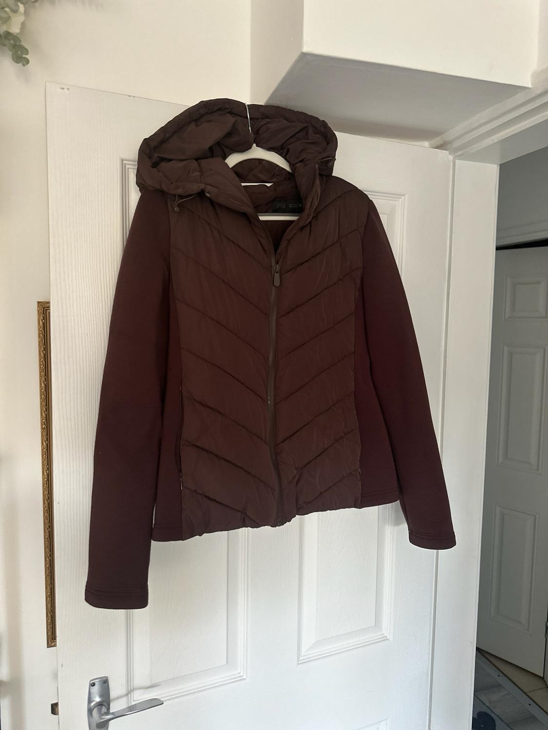 Dark brown jacket with a hood and padded front, hanging on a coat hanger over a white door.