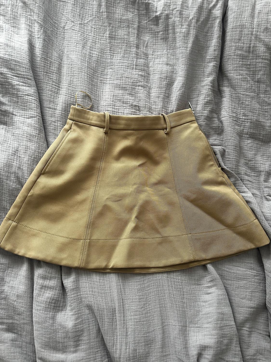 Short beige skirt on crumpled grey fabric. Design with visible seams and belt loops. Relaxed and casual vibe.