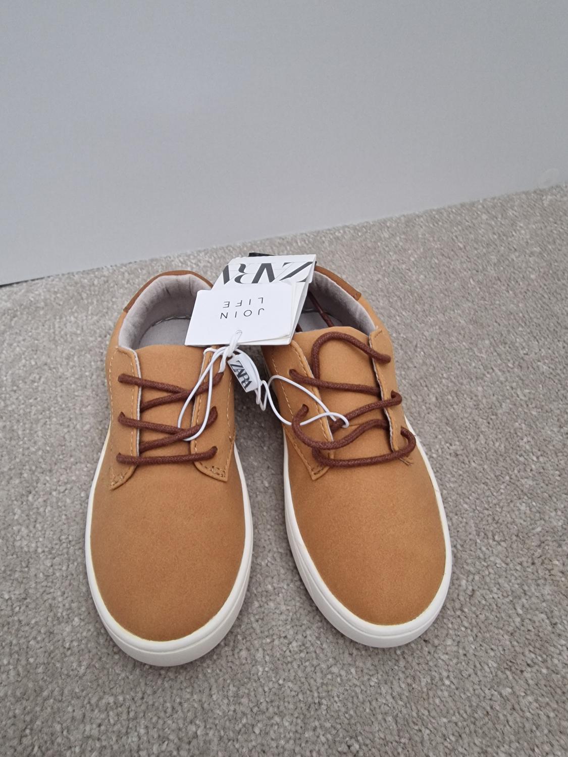 Brown shoes with dark laces on grey carpet. Visible label with text: "JOIN LIFE". White background.