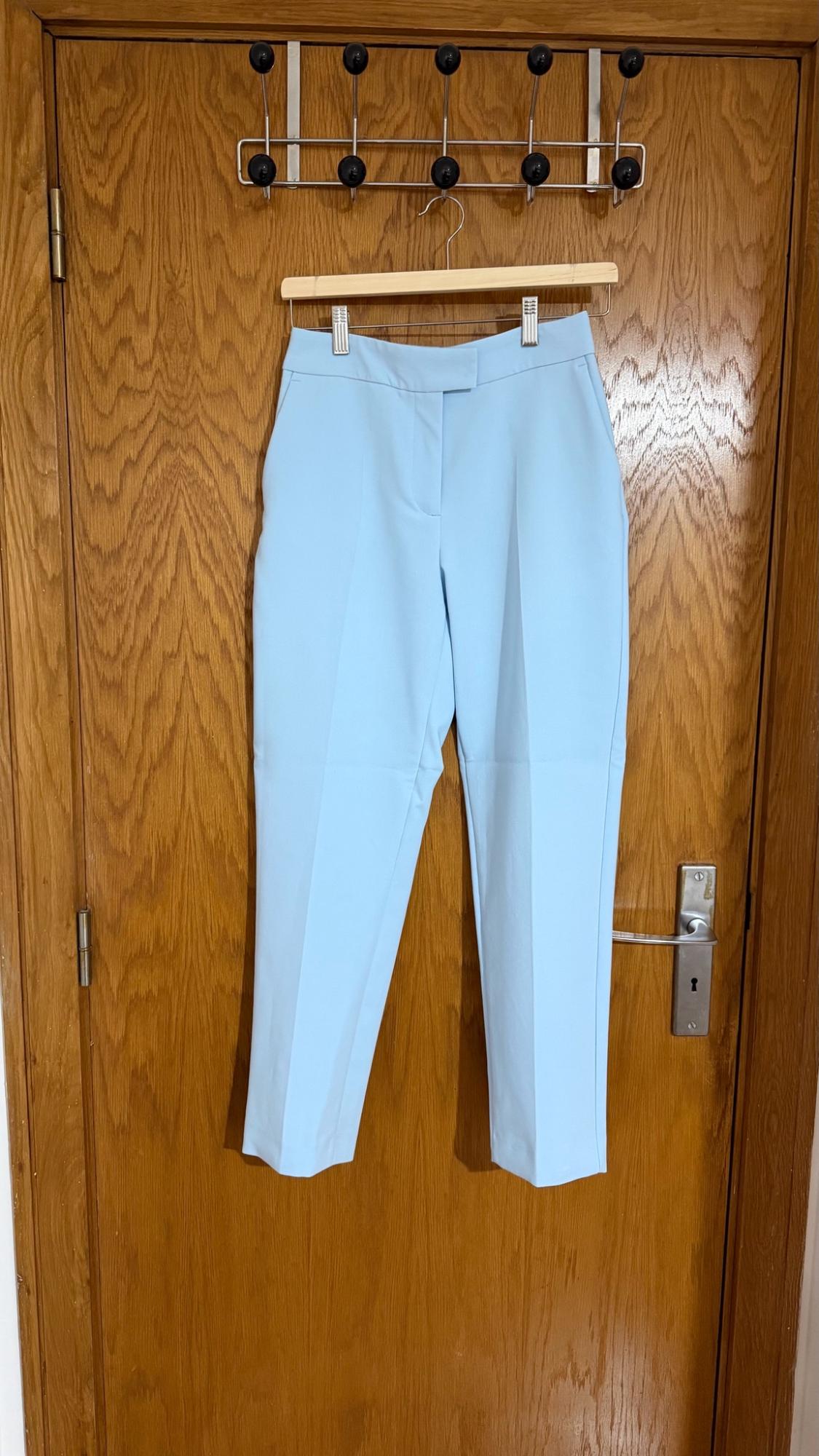Light blue trousers hanging on a wooden hanger on a wooden door with a metal coat rack.