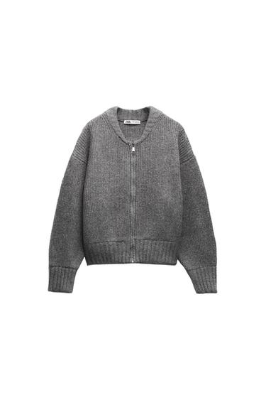 Gray knit jacket with front zipper and round neck, on a white background. Visible label on the inside of the collar.