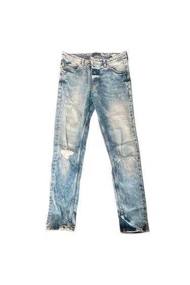 Light blue jeans with a washed and distressed effect, featuring rips at the knees and a button closure on a white background.