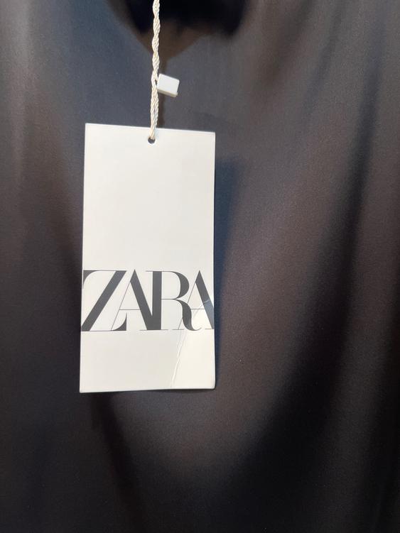 White tag with the text "ZARA" in black letters hanging over a dark background.