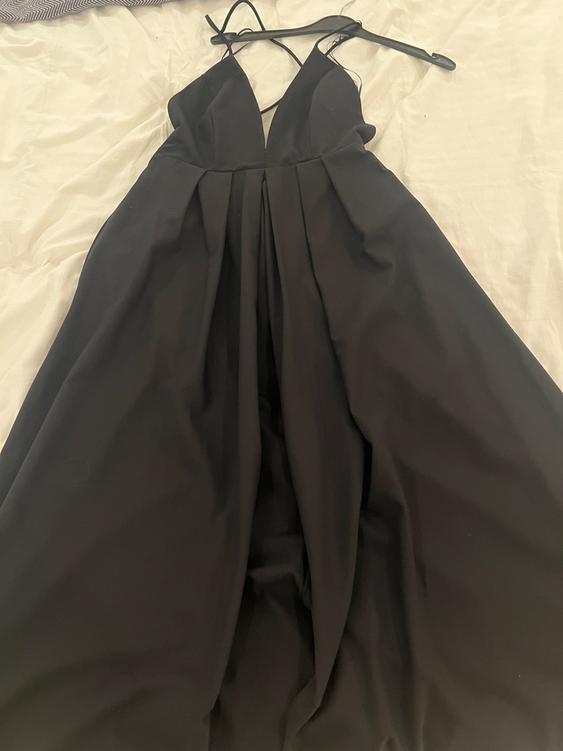 Black slip dress with a V-neckline, hanging on a hanger over a bed with light-coloured sheets.