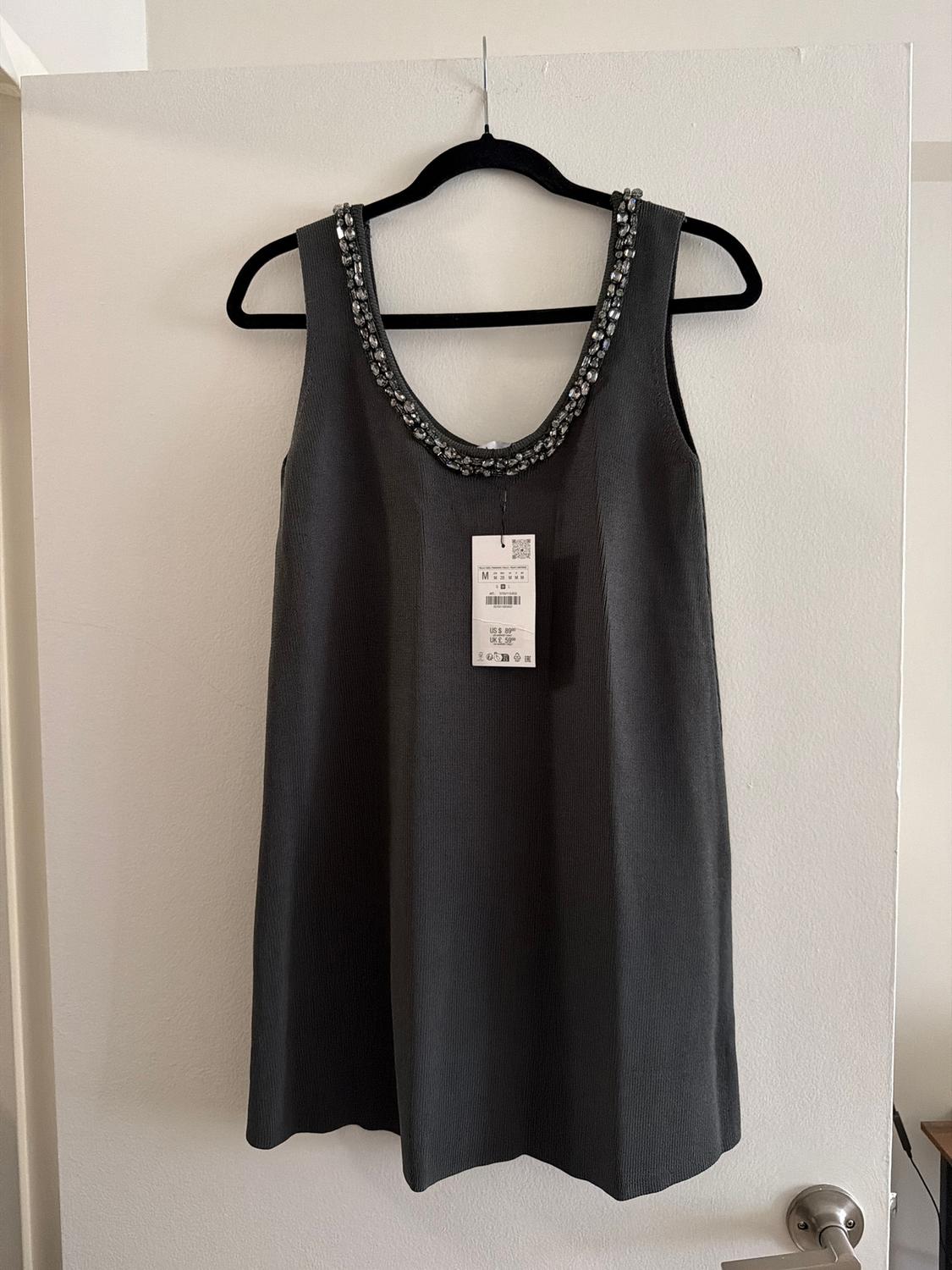 Sleeveless grey dress with a jewelled neckline, hanging on a black hanger. Label visible in the centre.