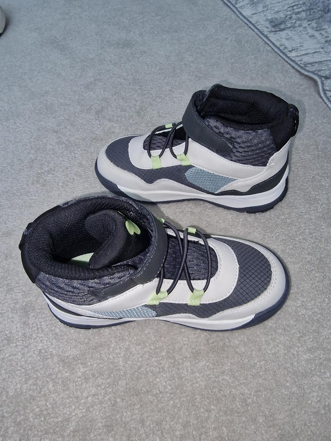 Trainers in shades of grey, white and black with green and blue detailing, on a light grey carpet.