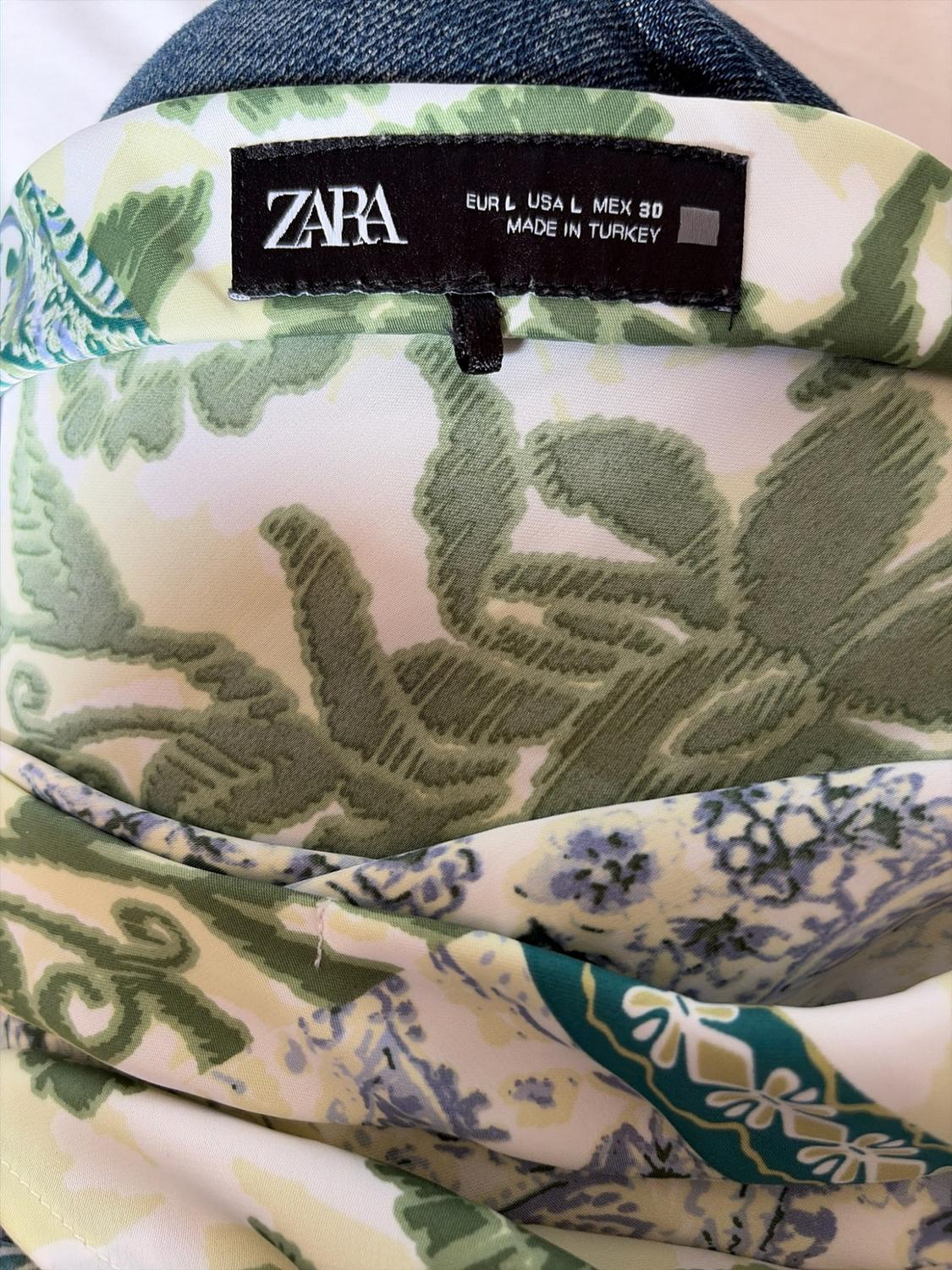 Black label with text ZARA EUR L USA L MEX 30 MADE IN TURKEY on a garment with a green and white floral print next to blue denim fabric.