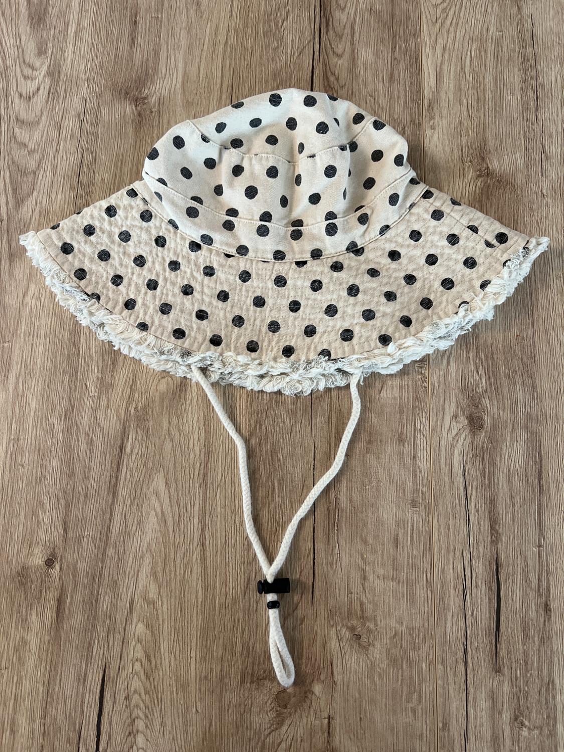 Beige fabric hat with black polka dots and adjustable drawstring, on a light wooden background.