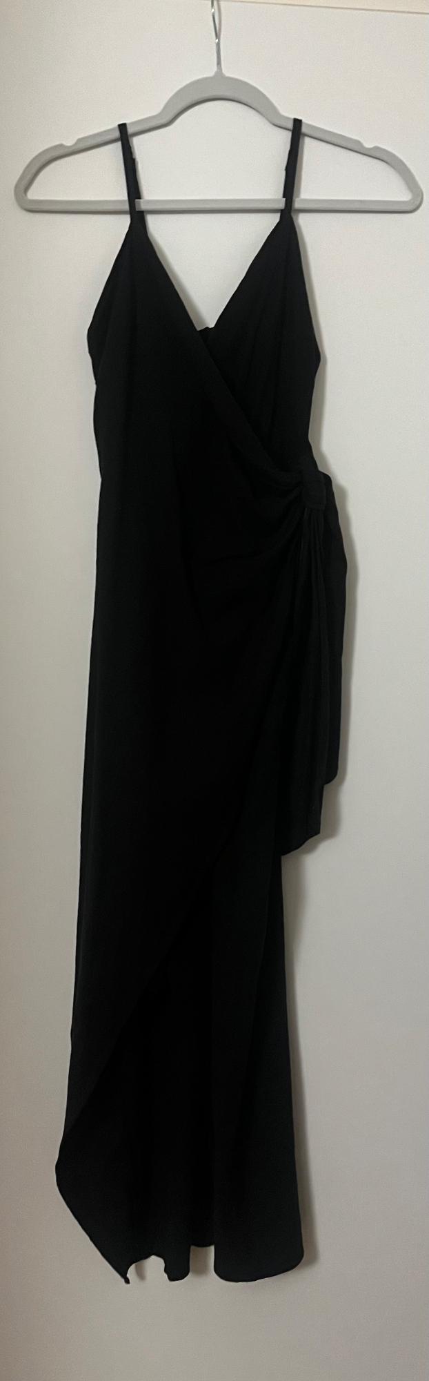 Black spaghetti strap dress hanging on a grey hanger. Asymmetrical design with side draping, white background.