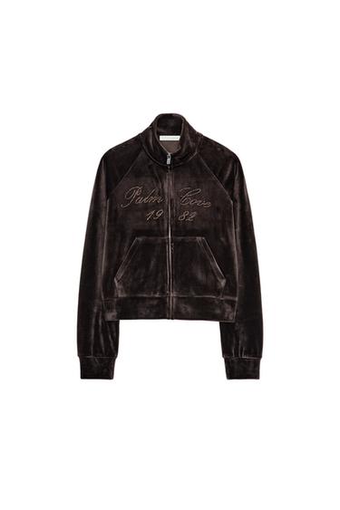 Front view of a brown jacket with a high collar, embroidered text "Palm Cove 1984", front pockets and zip fastening.