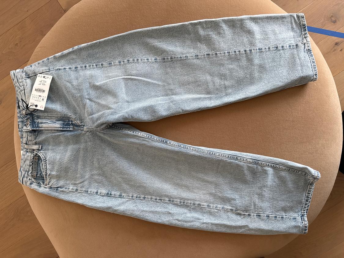Light blue jeans with a label on a beige sofa, on a light wooden floor.
