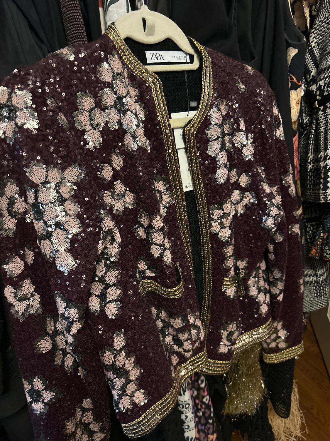 Burgundy sequin jacket with flowers and gold details, hanging on a clothes rack. Visible tag with the text "ZARA".