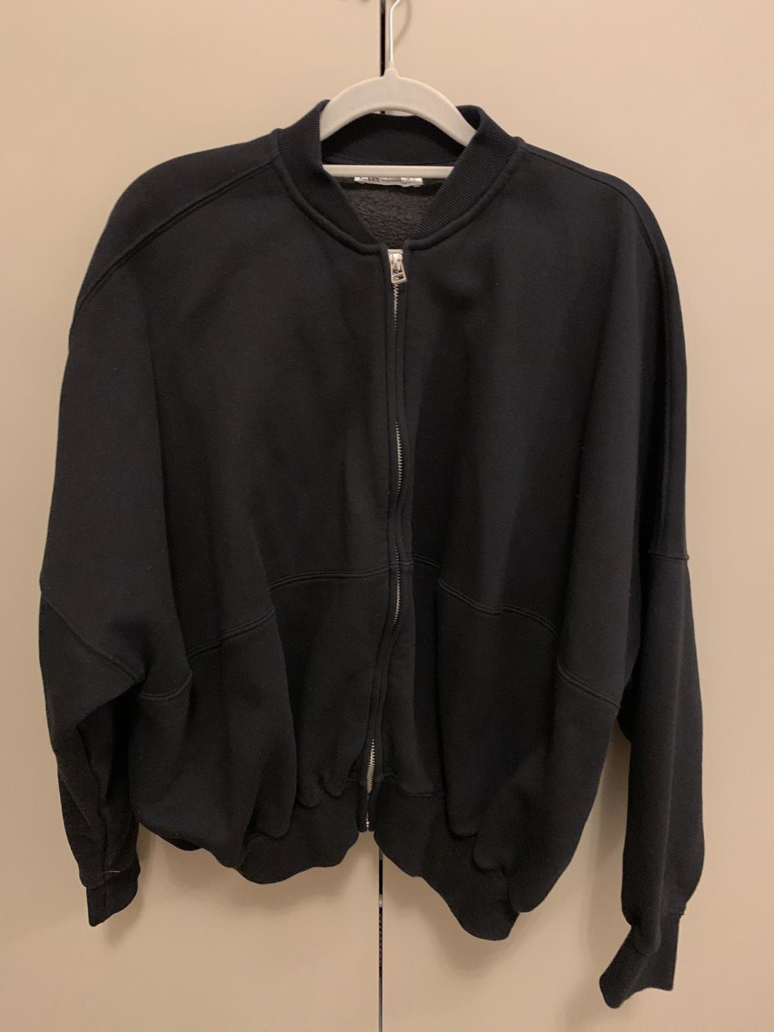 Black zip-up jacket hanging on a white hanger against a beige background. Simple and casual design.