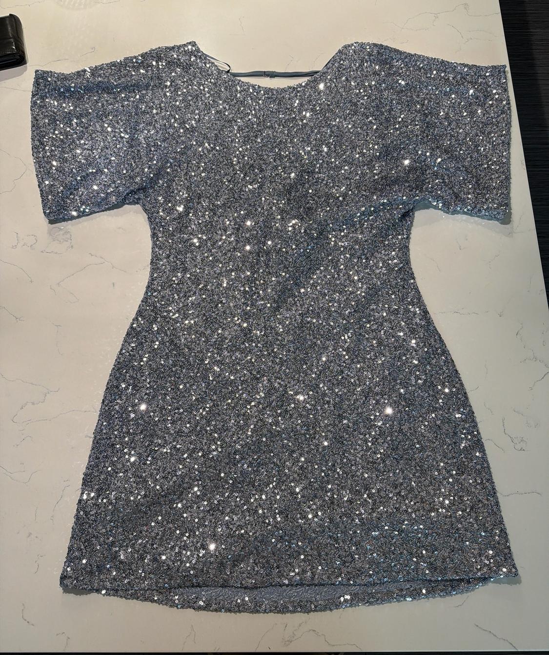 Short-sleeved silver sequin mini dress on a white marble surface. Relaxed, festive-style composition.