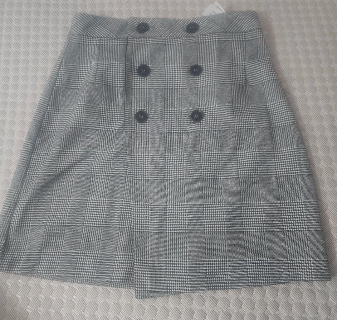 Grey plaid mini skirt with black buttons on the front, on a light-toned textured surface.