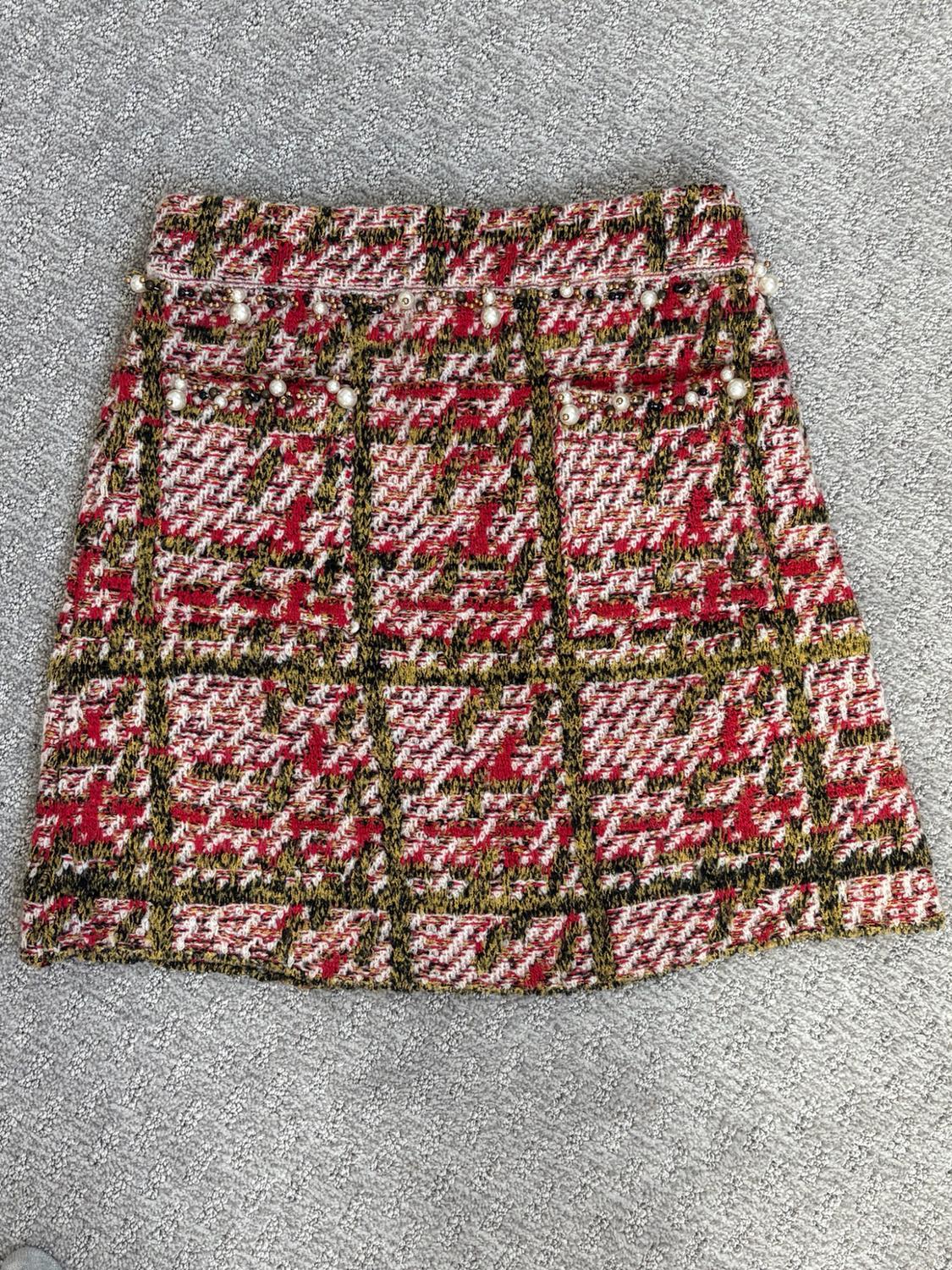Plaid knit mini skirt in red, white, and black tones with pearl details, photographed on a gray rug.