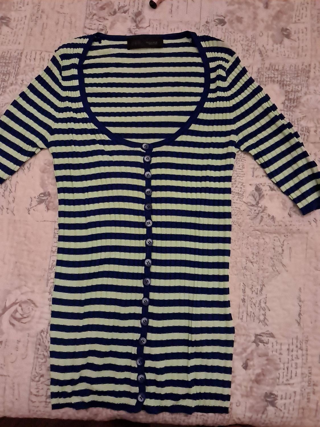 Navy blue and light green ribbed top with horizontal stripes, a round neckline and front buttons, against a patterned background.