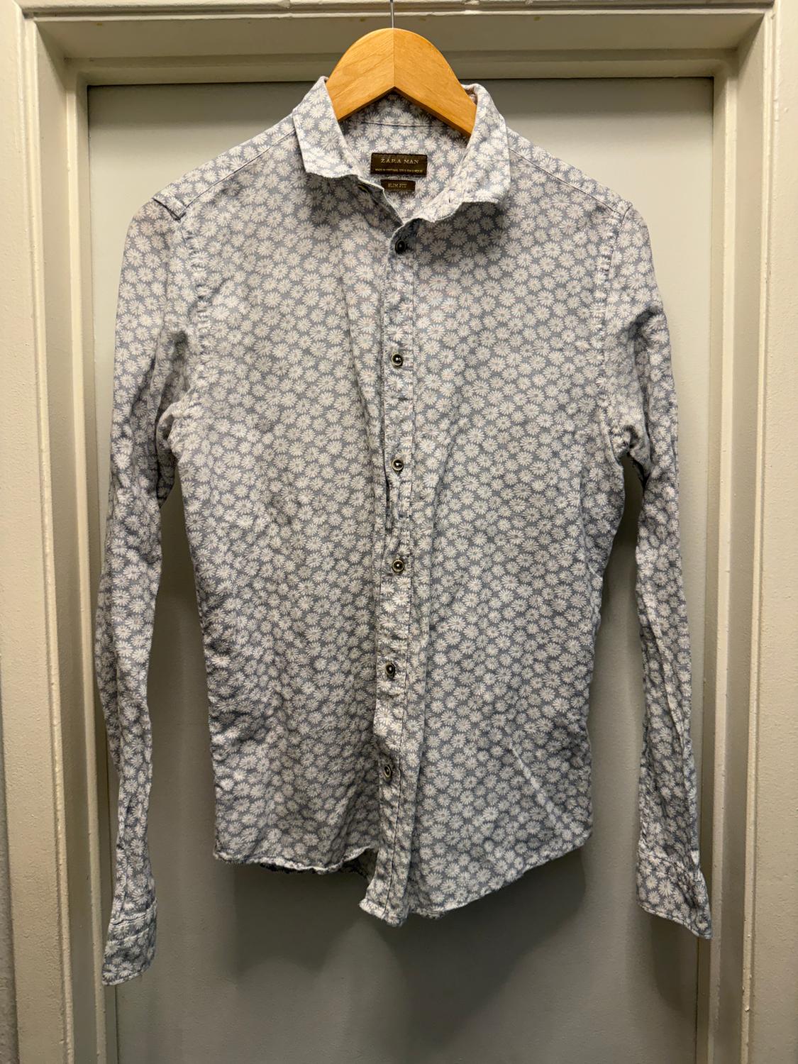 White and blue floral long-sleeved shirt, hanging on a wooden hanger over a white door.